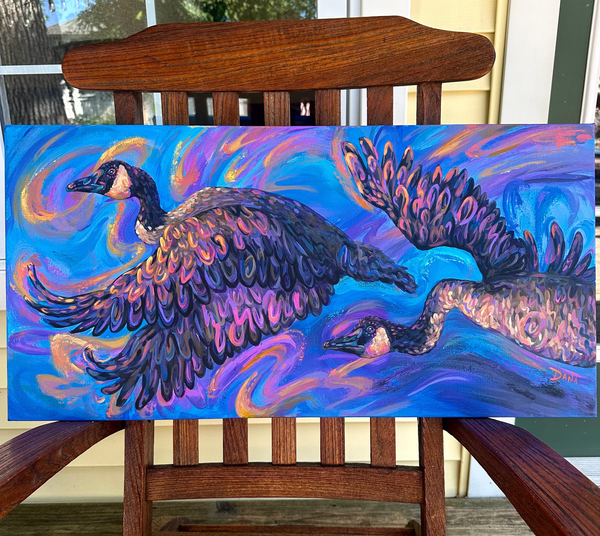 Colorful painting of two geese chasing the sunset. Painting on a wooden chair outdoors